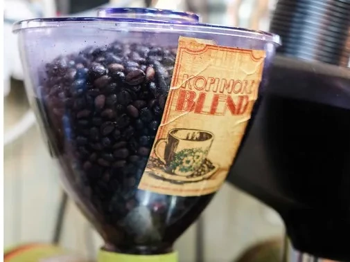 The grinder hopper with the KOPI MORE BLEND kraft label