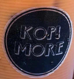 The round KOPI MORE sticker on a takeaway cup