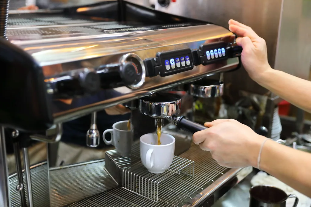 Kopi pouring from the group head into porcelain cups